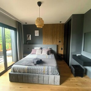 Ein modernes Schlafzimmer mit einem großen Bett, einer Hängeleuchte und Blick ins Freie.
