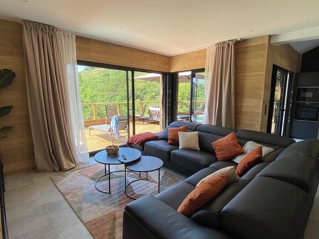Un saló modern amb un sofà modular, una taula rodona petita i una gran porta corredissa de vidre que dona a una zona exterior amb una piscina.