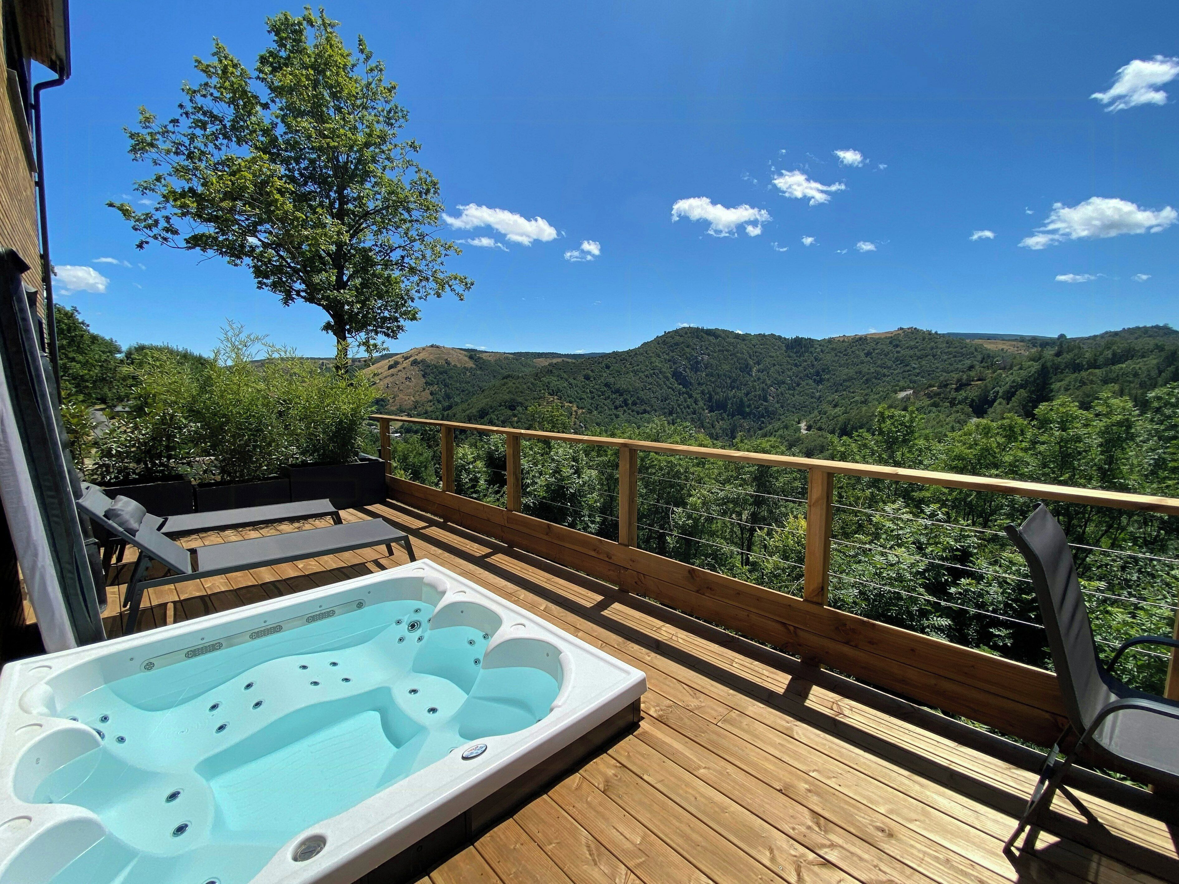 Una terraza de madera con un jacuzzi y sillones de descanso, con vista a un valle boscoso.