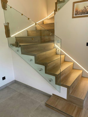 Eine moderne Treppe mit Glastrennläufen und Holzstufen, die zu einer Empore mit einem gerahmten Bild führt.