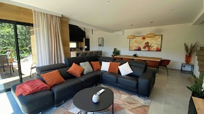 Ein modernes Wohnzimmer mit Ecksofa, einem Essbereich und einer Küche im Hintergrund.