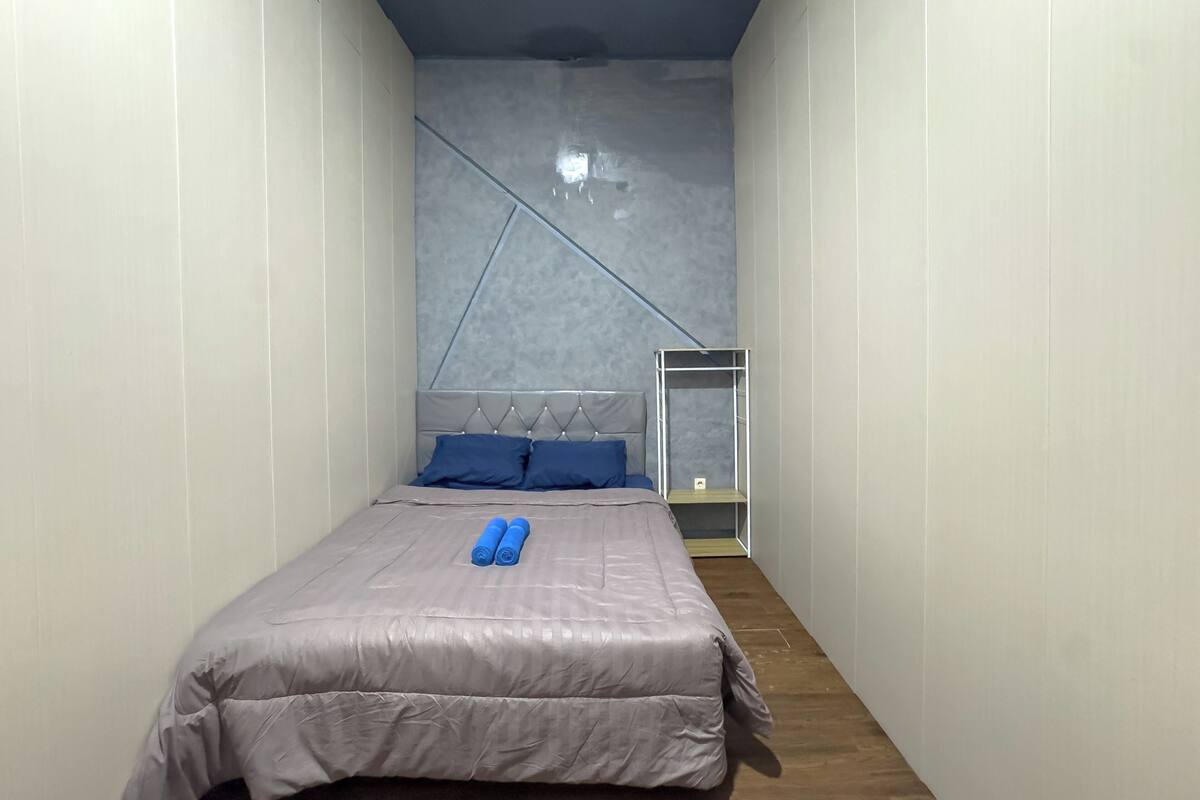 A narrow room with a bed, a headboard, and a small shelf.