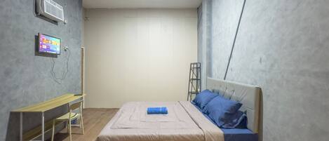 A bedroom with a bed, a desk, a chair, a TV, and an air conditioning unit.