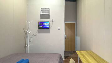 Una habitación de hotel con cama, escritorio, televisor montado en la pared y aire acondicionado.