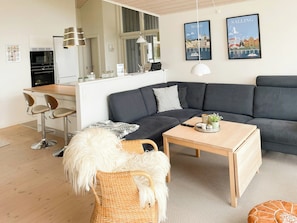 A modern living room with a grey sectional sofa, a wooden coffee table, a wicker chair, and a small rug. - Stunning sunrises over Harre Vig (Roslev)