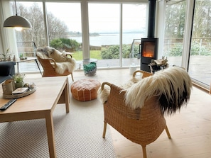 A modern living room with a large window, a fireplace, wicker furniture, and a view of the outdoors. - Stunning sunrises over Harre Vig (Roslev)