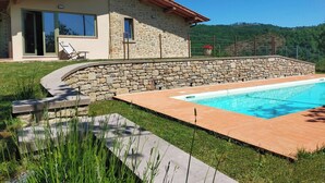 Ein Steinhhaus mit Swimmingpool, Steinmauer und Rasenfläche.