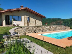 Ein Steinhhaus mit Swimmingpool, Steinmauer und Rasenfläche.