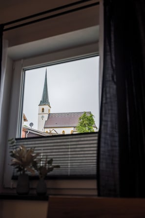 A window with a view of a building with a spire and a clock. - Vacation apartment M3 for 4 persons (Taching am See)