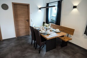 A dining area with a wooden table set for two, a bench, and a window with curtains. - Vacation apartment M3 for 4 persons (Taching am See)
