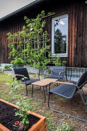 A wooden building with a window, a small tree, and outdoor furniture. - Vacation apartment M3 for 4 persons (Taching am See)