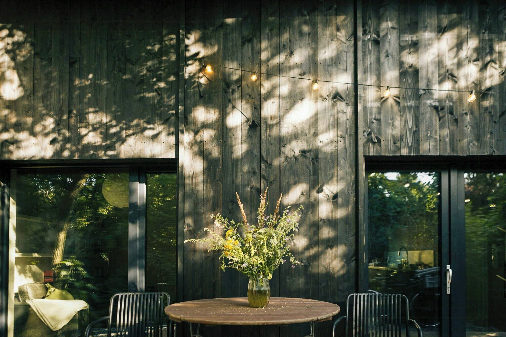 A round table with a vase of flowers, two chairs, and a view through large windows.