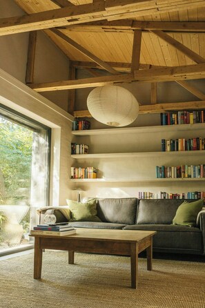 Ein gemütliches Wohnzimmer mit Holzboden, einer Couch, einem Couchtisch und Bücherregalen voller Bücher.