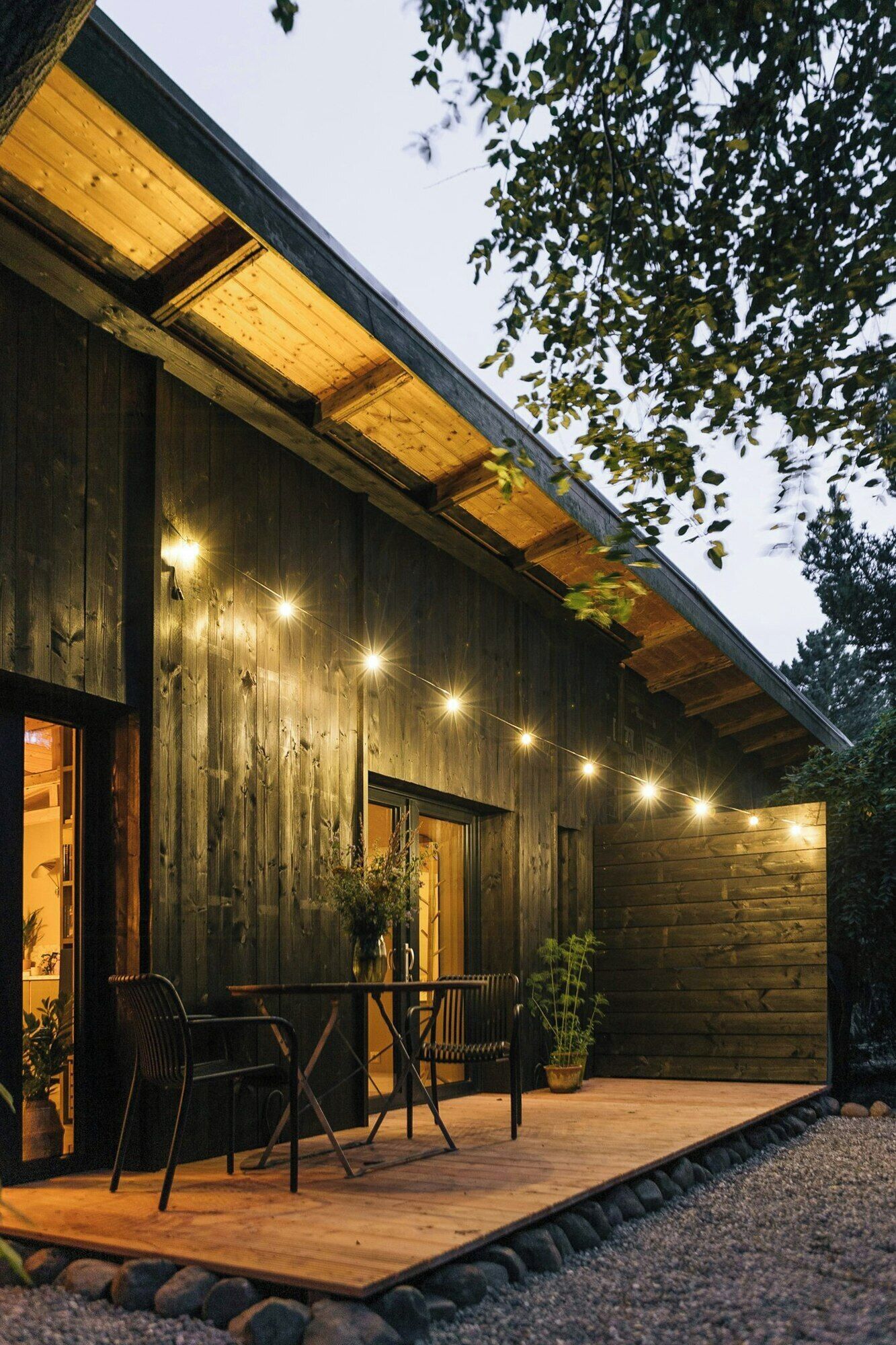 A wooden building with a covered porch, outdoor seating, and string lights.