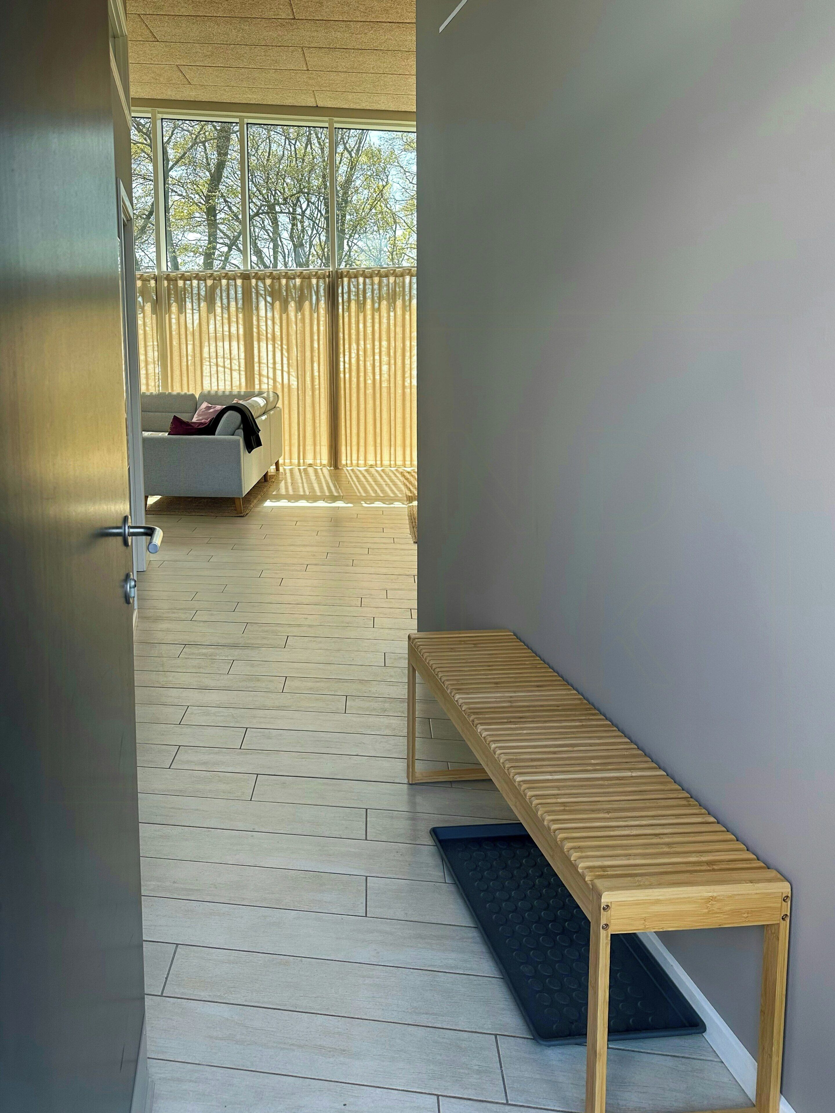 Un couloir avec un banc en bois, un canapé et une vue sur les arbres à travers de grandes fenêtres.