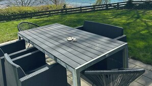 Un patio al aire libre con una mesa y sillas, vista a un lago y cielo despejado.