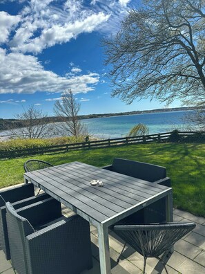 Eine Terrasse im Freien mit Tisch und Stühlen, Blick auf einen See und wolkenlosen Himmel.