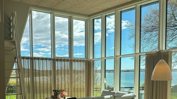 Un interior moderno con un ventanal grande, un sofá, una mesa de comedor y una escalera.