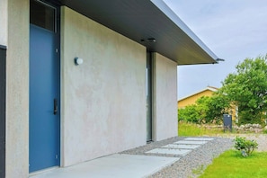 Un bâtiment moderne avec une porte bleue, une façade en béton et un chemin de gravier menant à l’entrée.
