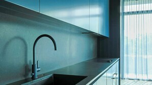 Eine moderne Küche mit Spüle aus Edelstahl, einem Bogenarmaturen-Wasserhahn und einem Fenster mit transparenten Vorhängen.