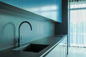 Une cuisine moderne dotée d’un évier en acier inoxydable, d’un robinet au design incurvé et d’une fenêtre ornée de rideaux légers.