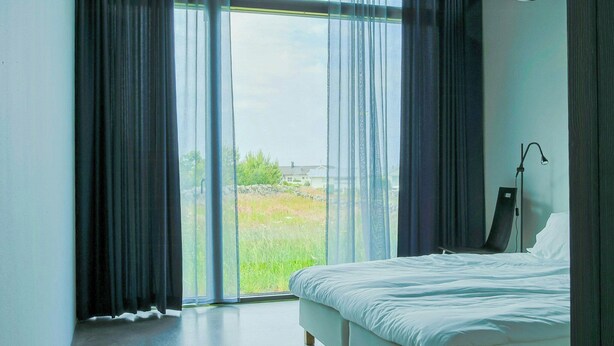 Ein Schlafzimmer mit einem großen Bett, einer Stehlampe und Blick durch eine Glastür.