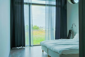 Un dormitorio con una cama grande, una lámpara de pie y vistas a través de un ventanal.