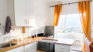 Una cocina compacta con gabinetes blancos, microondas integrado y una ventana con cortinas.