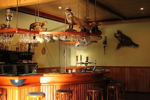 Eine Bar mit Holztresen, Hockstühlen und einem Regal mit dekorativen Tierfiguren.