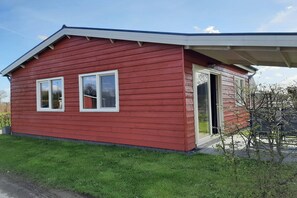 A small, single-story red wooden house with a covered porch, a door, and two windows.