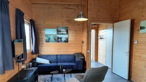 Interior de una cabaña de madera con un sofá, una silla, una mesa, una lámpara y una luz en el techo.
