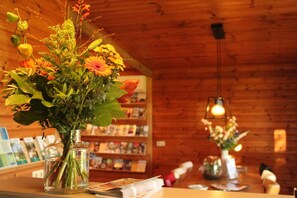 A wooden interior with a wooden bookshelf, a table with a vase of flowers, and a hanging light fixture.