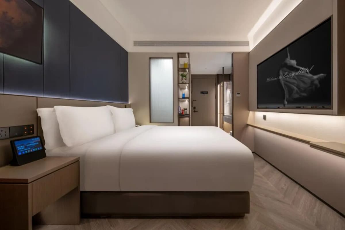 Une chambre d’hôtel moderne dotée d’un grand lit, d’un panneau de commande situé près du lit, d’un téléviseur fixé au mur et d’une porte donnant accès à la salle de bain.