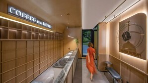 Un moderno vestíbulo de hotel con una barra de café, una zona de estar y un reloj montado en la pared.