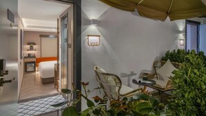 Una habitación de hotel con cama, una mesita, una silla de mimbre y una planta en maceta.