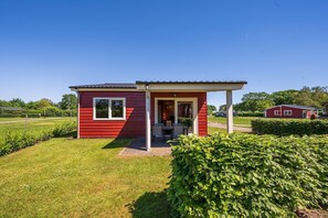 A small red building with a covered porch and a window, surrounded by greenery. - Country Holiday home with shared pool (Someren-Heide)