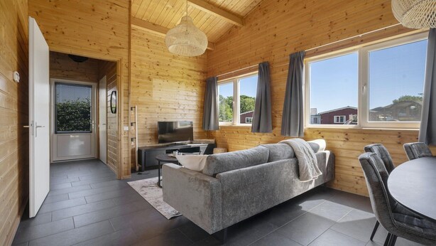 Un interior de madera con sofá, mesa de comedor, televisor y ventanas amplias.