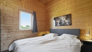 Habitación con paneles de madera, una cama, una ventana con cortinas, un cuadro en la pared y una mesita de noche con lámpara.