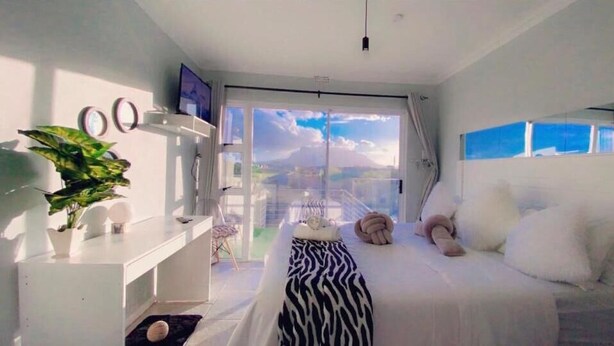 A bedroom with a bed, a TV, a plant, and a balcony with a view. - Quaaamiii Accomodation (Cape Town)