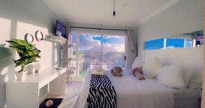 Un dormitorio con cama, televisión, planta y balcón con vistas.