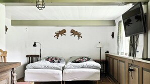 Um quarto com cama, escrivaninha, cadeira, luminária e televisão fixada na parede.