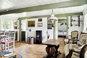 A cozy room with a fireplace, wooden furniture, and wall-mounted shelves. - Unique summer house with seaweed roof on Læsø (Læsø)