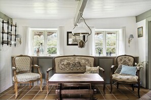 A room with a large window, a hanging light fixture, and two upholstered chairs with patterned cushions. - Unique summer house with seaweed roof on Læsø (Læsø)