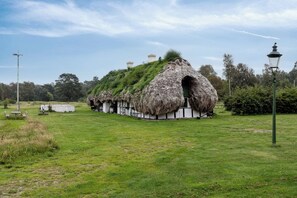 A thatched-roof structure with a grassy roof, surrounded by a grassy field and trees. - Unique summer house with seaweed roof on Læsø (Læsø)