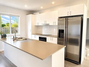 A modern kitchen with white cabinets, a stainless steel refrigerator, and a large island with a sink. - No.22 4B Pimpama Home (Pimpama)
