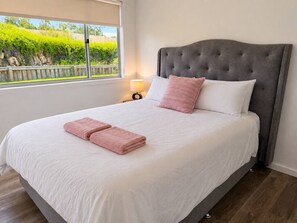 A neatly made bed with a grey headboard, white bedding, and pink towels.