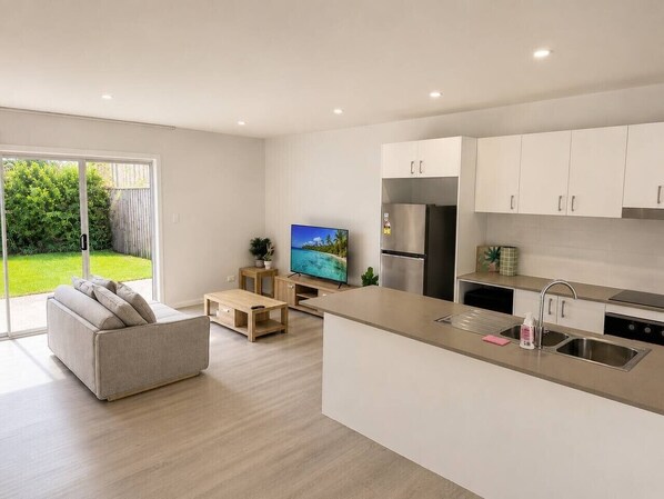 A modern kitchen with white cabinets, a stainless steel refrigerator, and a built-in island with a sink. - No. 19 3B Pimpama Home (Pimpama)