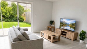 En moderne stue med sofa, sofabord, TV-møbel og udsigt til en have.