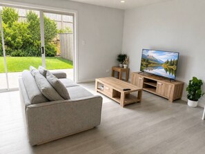 A modern living room with a sofa, coffee table, TV stand, and a view of a garden. - No. 19 3B Pimpama Home (Pimpama)