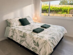 A bed with a floral bedspread, two pillows, and two folded towels. - No. 19 3B Pimpama Home (Pimpama)